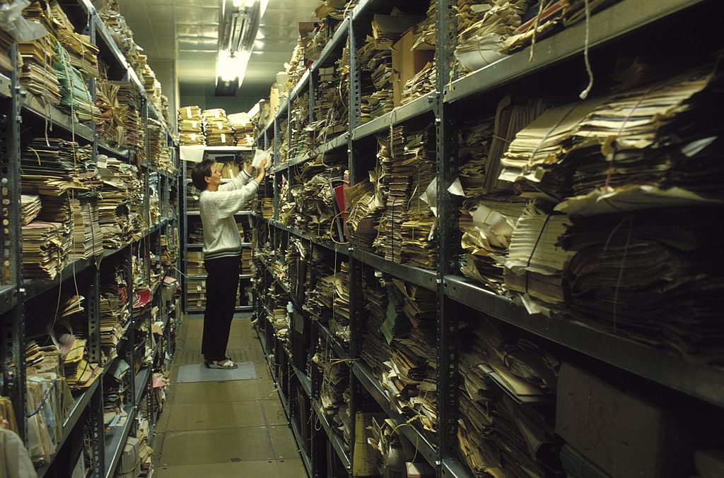 Ein Mann in einem Gang zwischen stark gefüllten Akten eines Archivs
